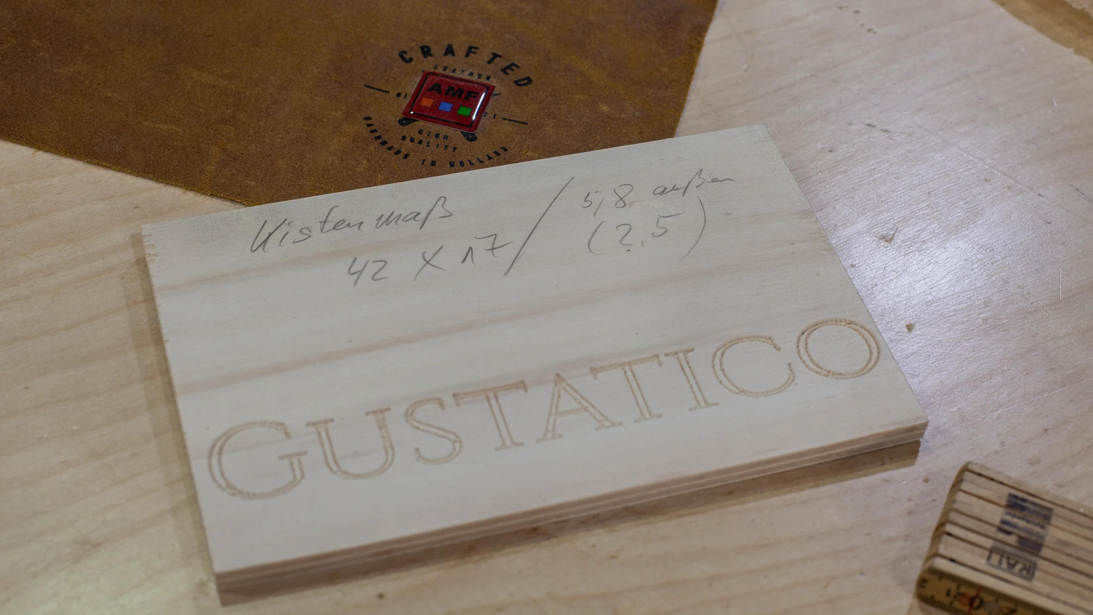 Schneidebrett mit eingraviertem GUSTATICO Schriftzug neben einem Maßzettel